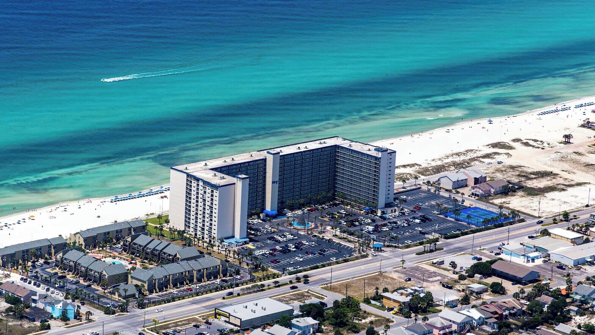 Vista aérea de um hotel com estacionamento, praia e estrada.
