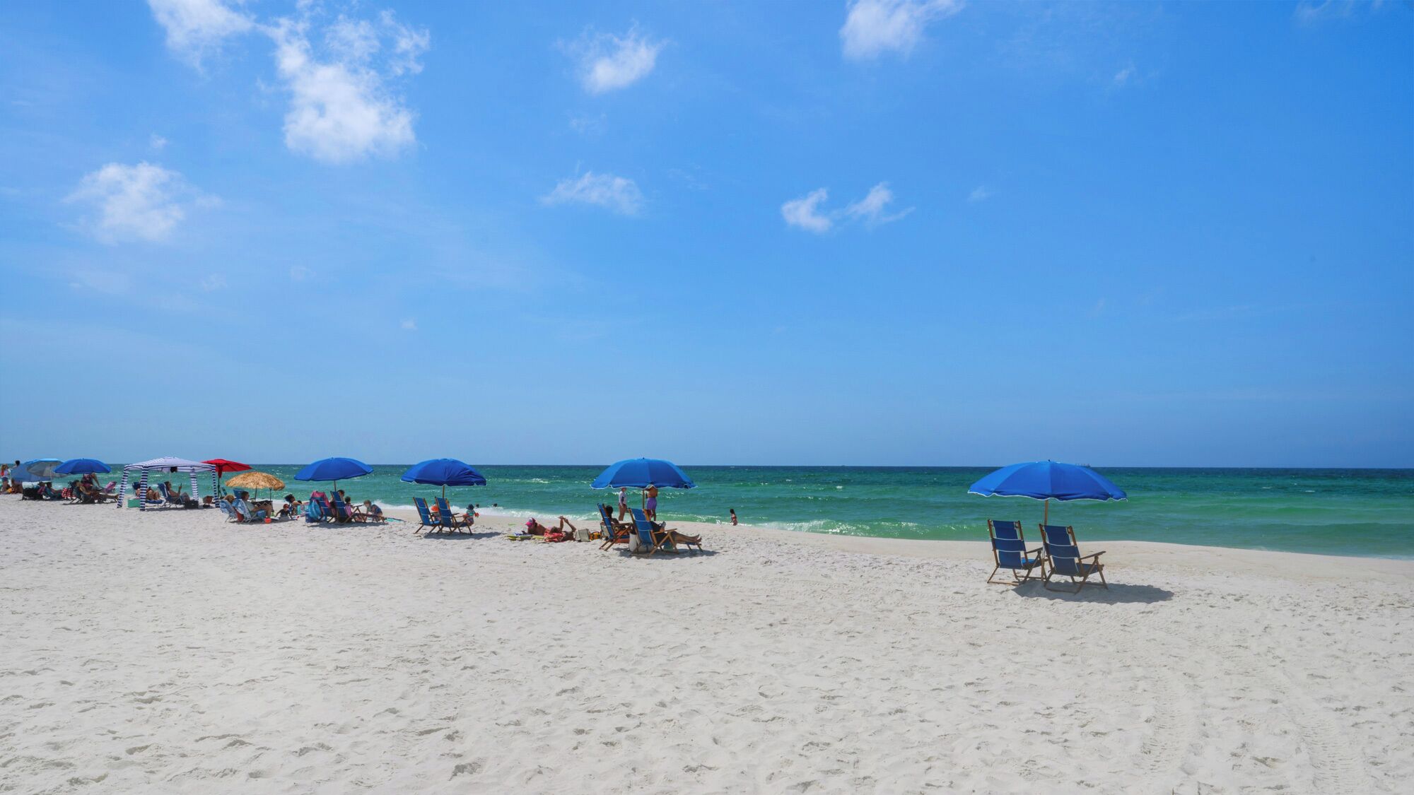 Een strand met rijen ligbedden en parasols onder een heldere lucht.