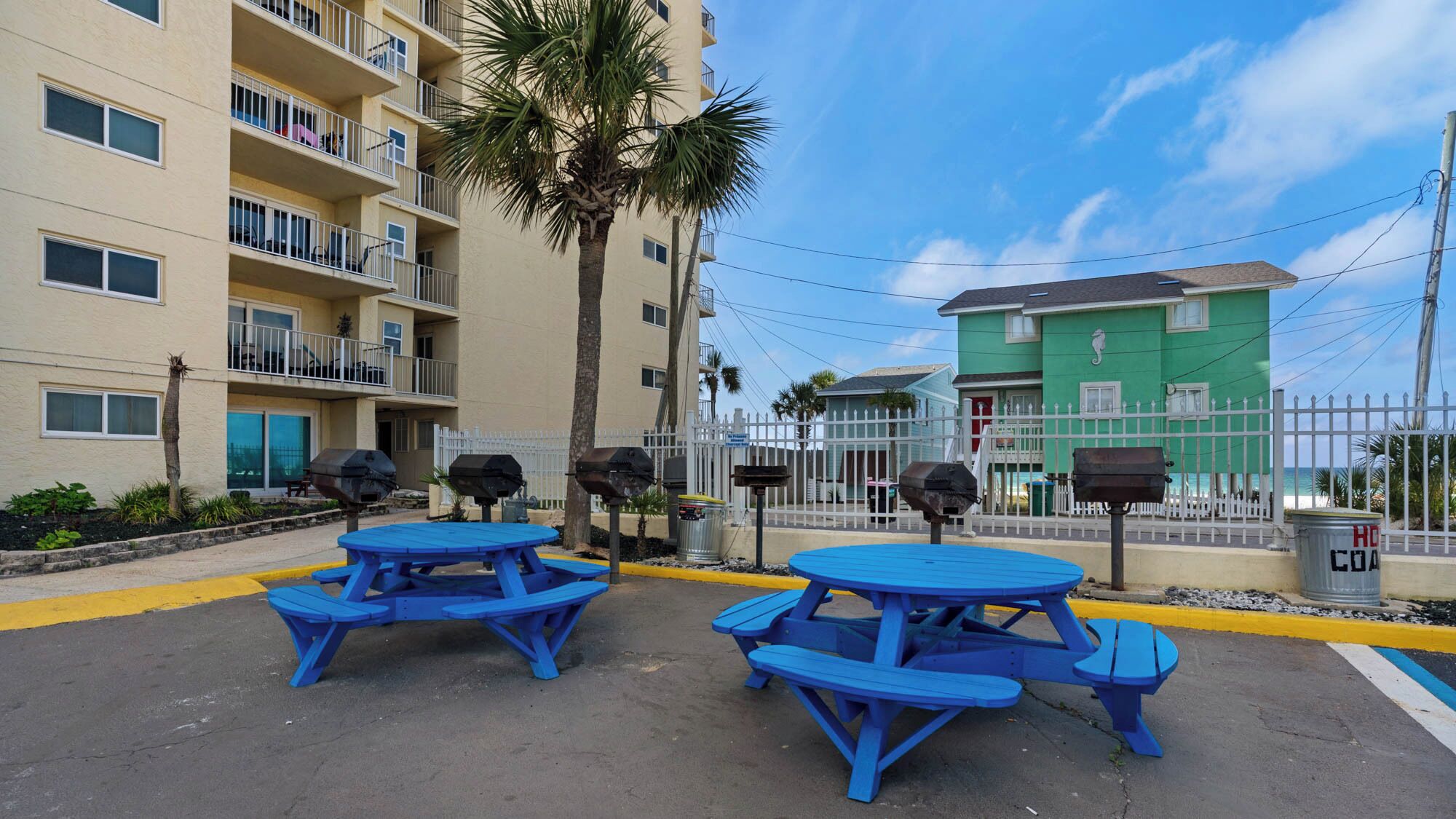 A parking area with blue picnic tables and barbecue grills.