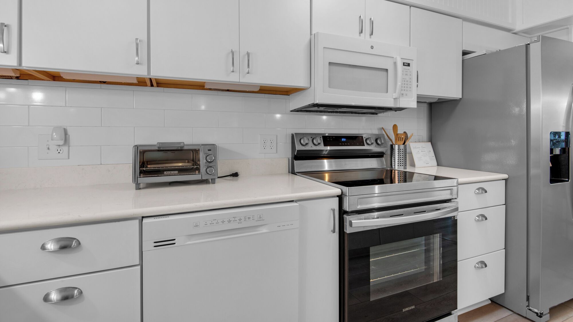 A modern kitchen with white cabinetry, a built-in microwave, a stainless steel oven, a dishwasher, and a refrigerator.