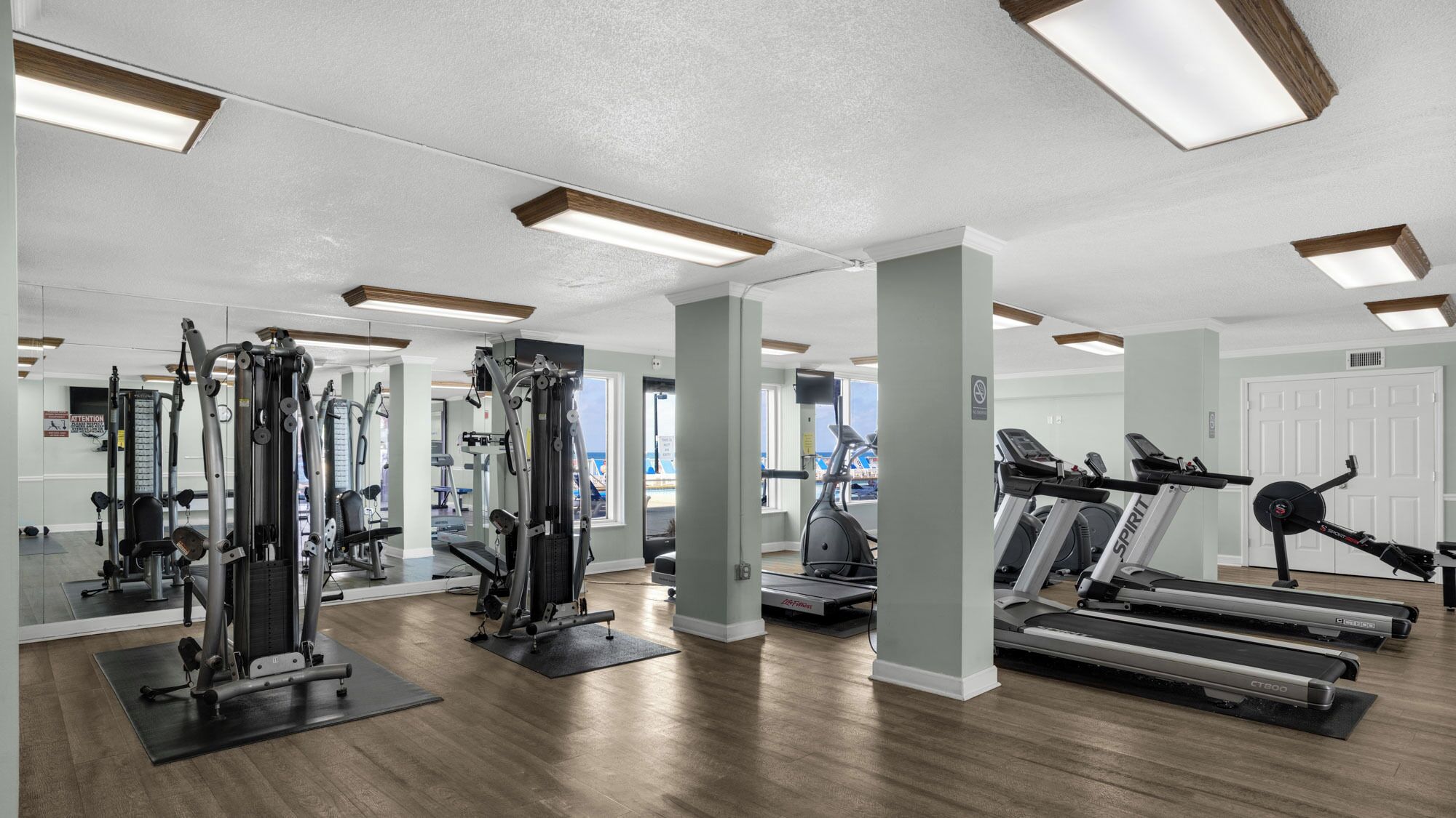 Uma academia com diversos equipamentos de exercício, incluindo esteiras e aparelhos de musculação, e um espelho grande que reflete o espaço.