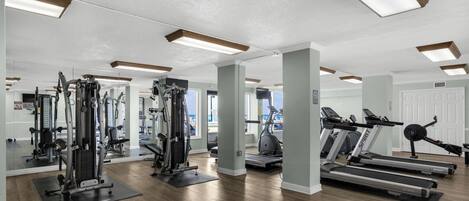 A gym with various exercise equipment, including treadmills and weight machines, and a large mirror reflecting the space.