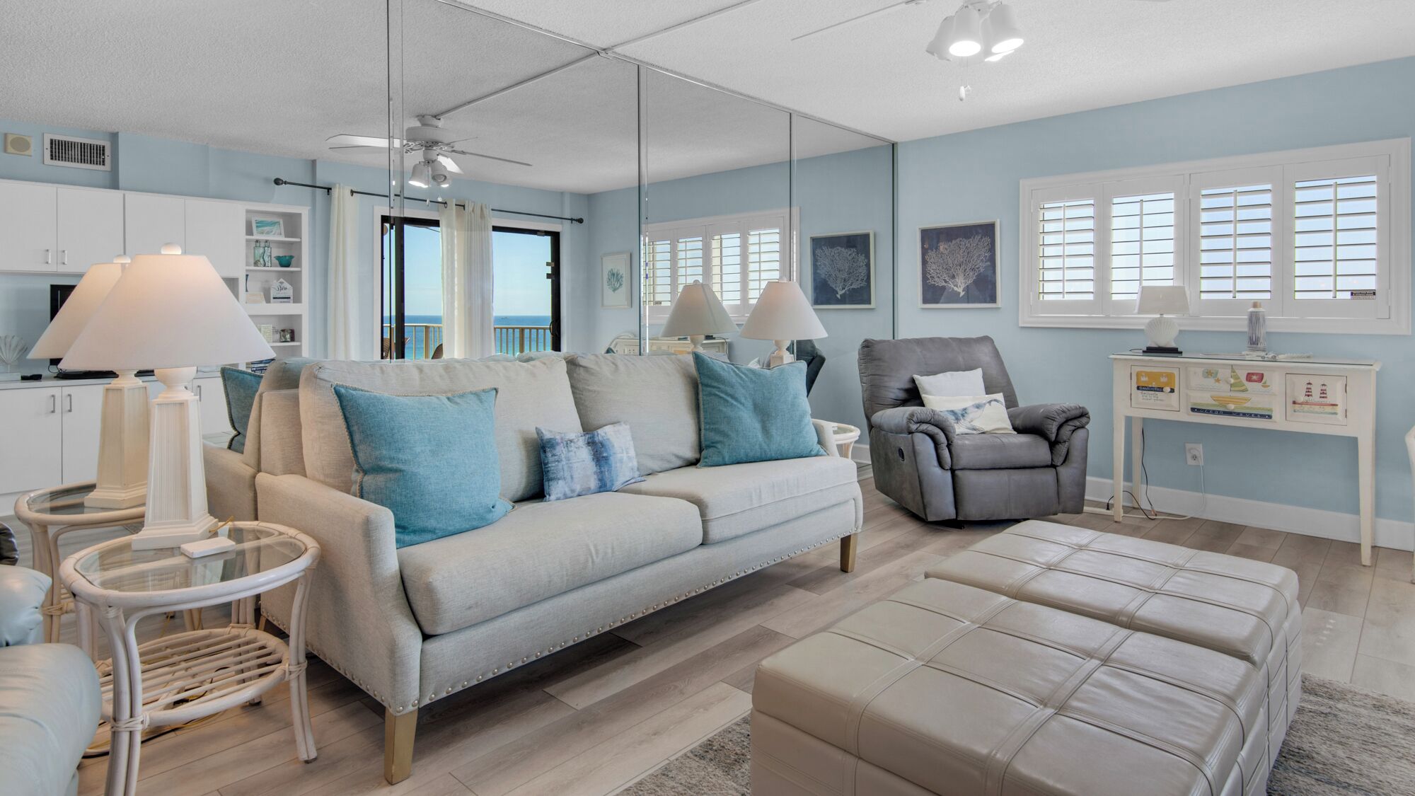 A modern living room with a sofa, armchair, and ottoman, a glass coffee table, and a side table with lamps.