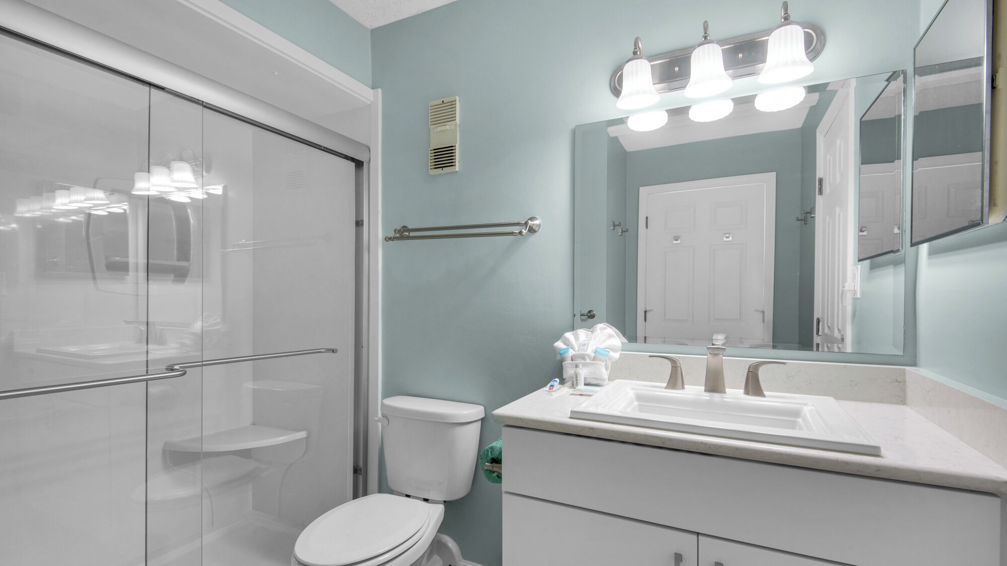Un baño moderno con cabina de ducha de vidrio, inodoro, lavamanos con espejo y perchero para toallas.