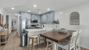 A modern kitchen with light blue cabinets, stainless steel appliances, and a wooden dining table with white chairs. - Gulf-front in Destin! Community Pool, Minutes to Beach (Destin)