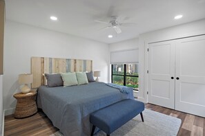 A bedroom with a bed, bedside lamps, a ceiling fan, a window, and a wardrobe.