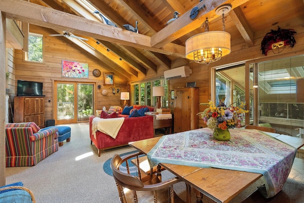 Interior acogedor de una cabaña con mesa de comedor, sofá rojo y vigas de madera.