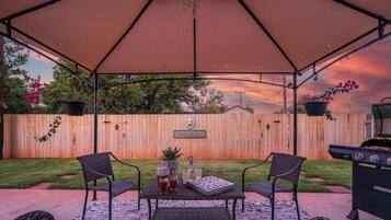 Un patio al aire libre con un espacio de estar techado, cerca de madera y una parrilla.
