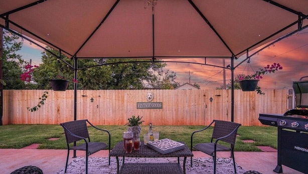Un espace extérieur aménagé en patio, doté d’un coin salon couvert, d’une clôture en bois et d’un barbecue.