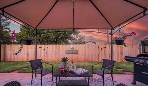 Un patio al aire libre con un espacio de estar techado, cerca de madera y una parrilla.