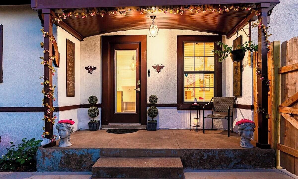 A porch with a wooden door, potted plants, and a chair.