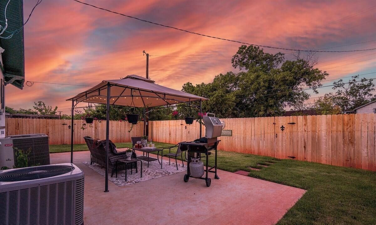 A backyard with a covered patio, outdoor furniture, a grill, and a wooden fence.