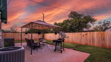 A backyard with a covered patio, outdoor furniture, a grill, and a wooden fence.