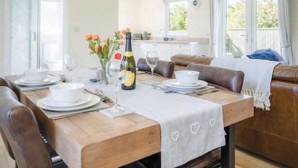 Un coin repas avec une table en bois dressée pour quatre personnes, une bouteille de vin et un vase rempli de fleurs.