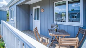 Un espace extérieur abrité, aménagé avec du mobilier en bois et une petite table, une porte et une fenêtre donnant sur le quartier.