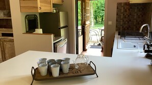 A kitchen with wooden cabinets, a refrigerator, a sink, and a tray with cups and a glass pitcher. - Maison de Campagne Rivière et Forêt (Le Brévedent)