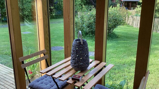 A wooden deck with a table and chairs, a decorative vase, and a book. - Maison de Campagne Rivière et Forêt (Le Brévedent)