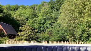 A swimming pool with a wooden fence and a building with a sloped roof in the background. - Maison de Campagne Rivière et Forêt (Le Brévedent)