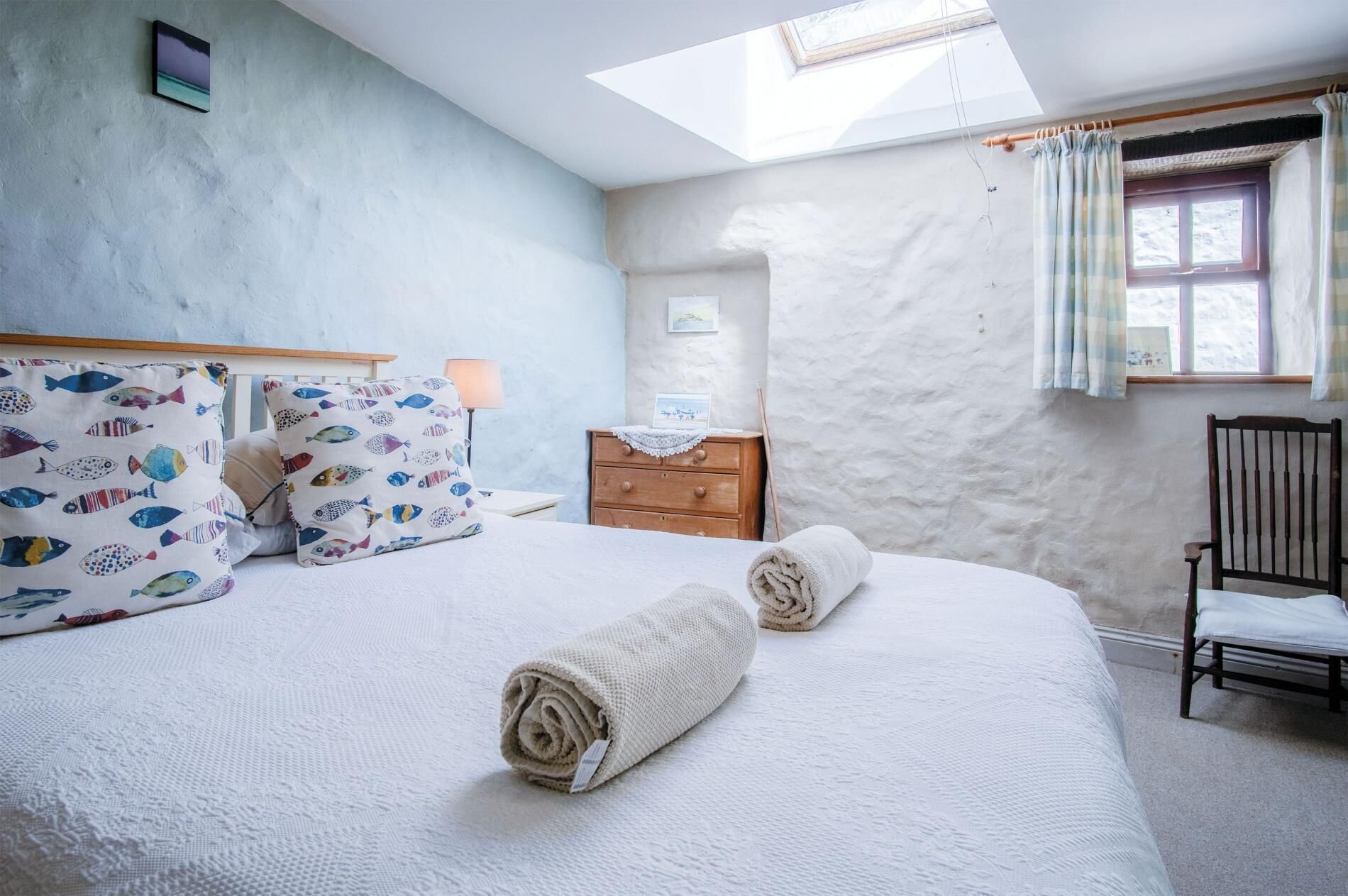 Een slaapkamer met een groot bed, een houten dressoir, een nachtkastje, een stoel en een dakraam.