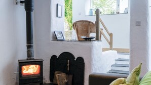 Une pièce chaleureuse avec un poêle à bois, un fauteuil en osier et un escalier menant à un niveau supérieur.