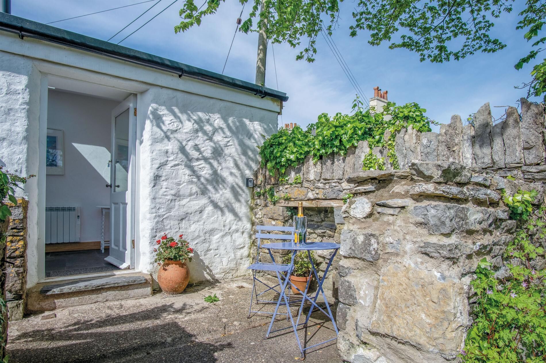 A stone wall with a small window, a white door, and a blue metal table with chairs.
