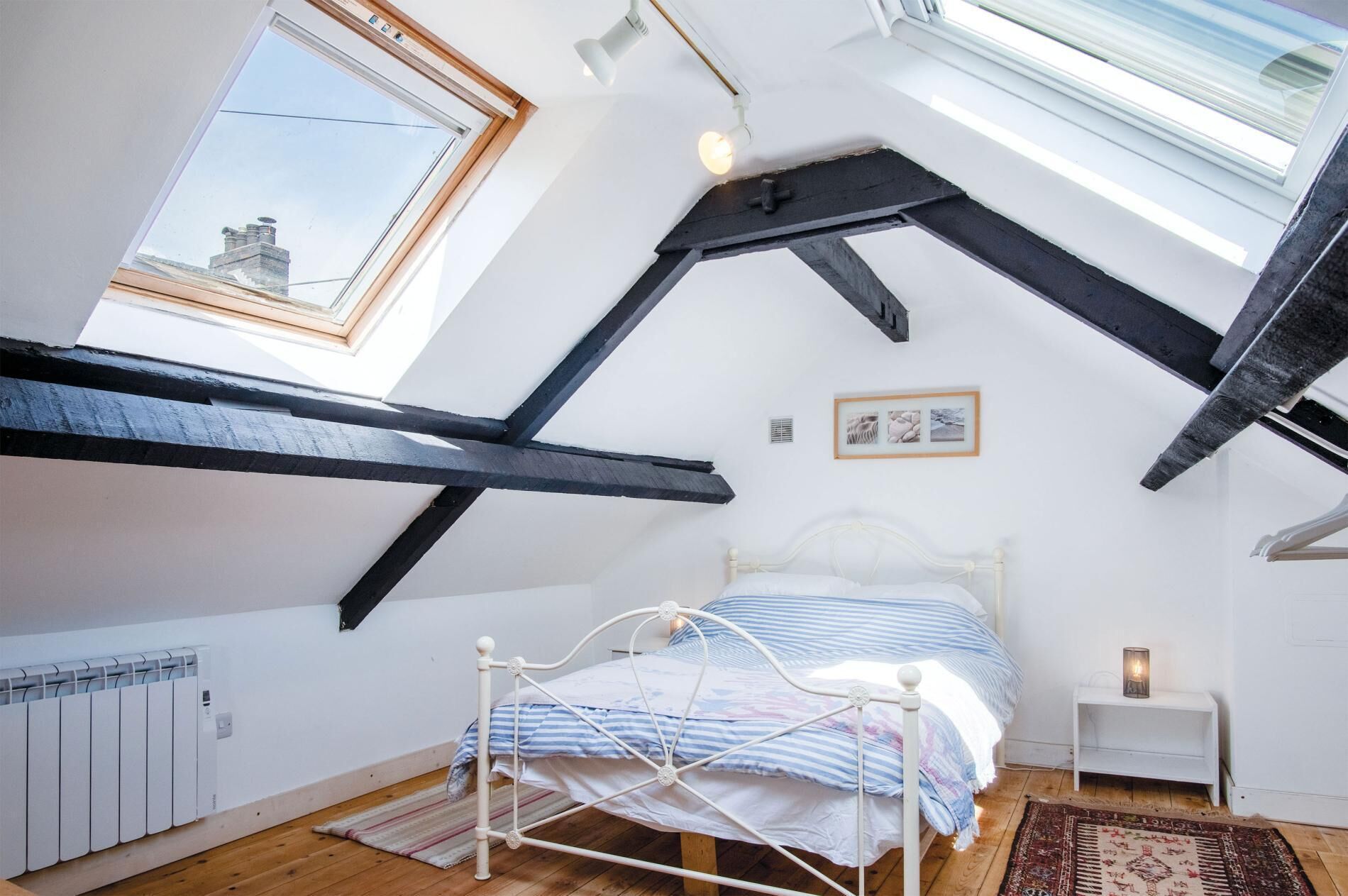 A bedroom with a sloped ceiling, a skylight, a bed, a radiator, and a small bedside table.