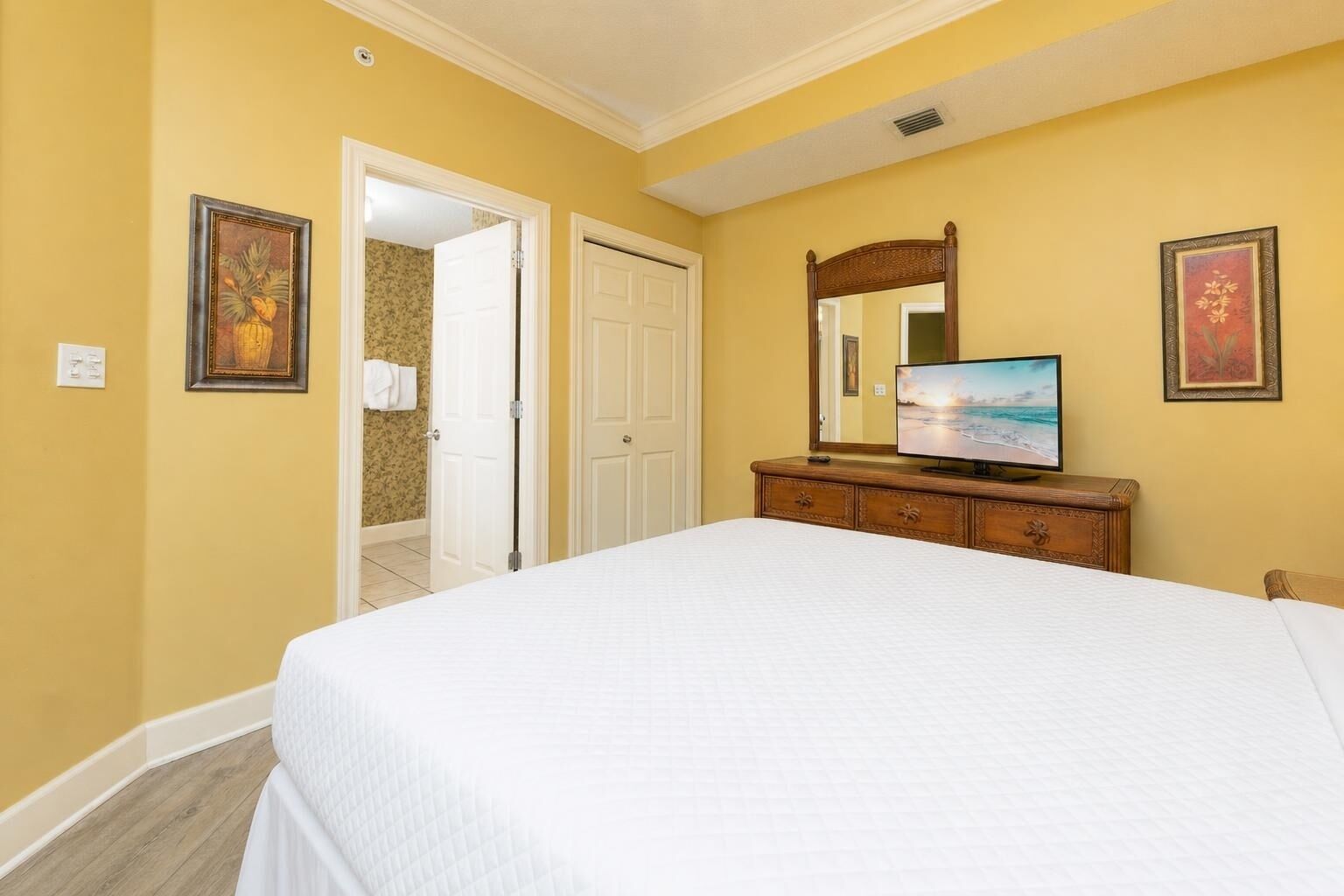 A bedroom with a bed, dresser, TV, and two doors leading to other rooms.
