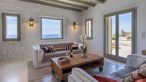Un salón espacioso con pared de piedra, una mesa de centro de madera, un sofá y grandes ventanales con vistas al exterior.