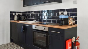Une cuisine avec des meubles de couleur sombre, un plan de travail en bois, un évier en acier inoxydable, un grille-pain, une bouilloire et une machine à café.