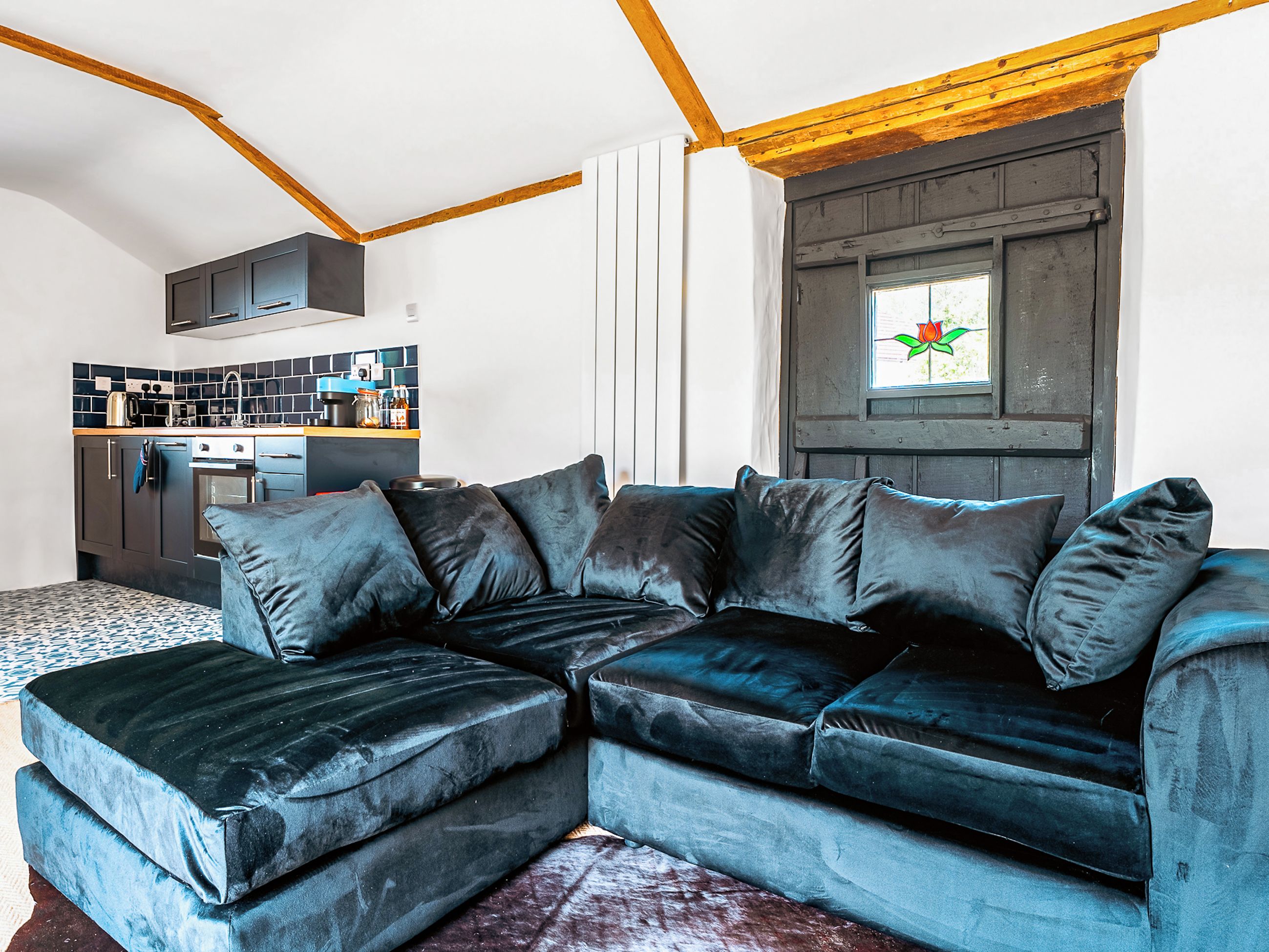 Een moderne woonkamer met een hoekbank, een keuken op de achtergrond en een raam met uitzicht op groen.