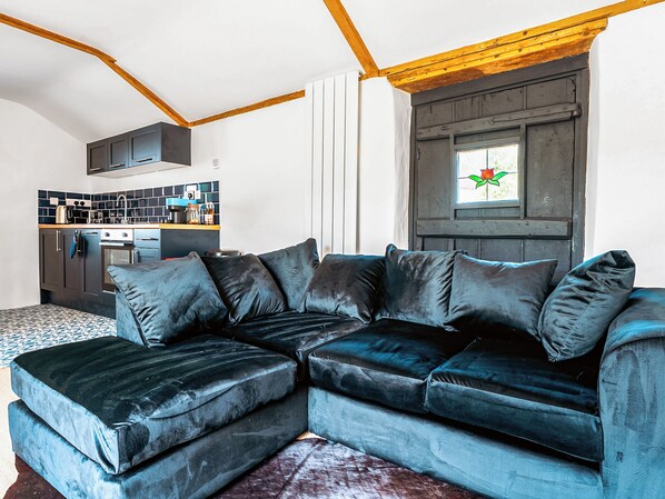 Un salon moderne avec un canapé d’angle, une cuisine en arrière-plan et une fenêtre donnant sur un paysage verdoyant.