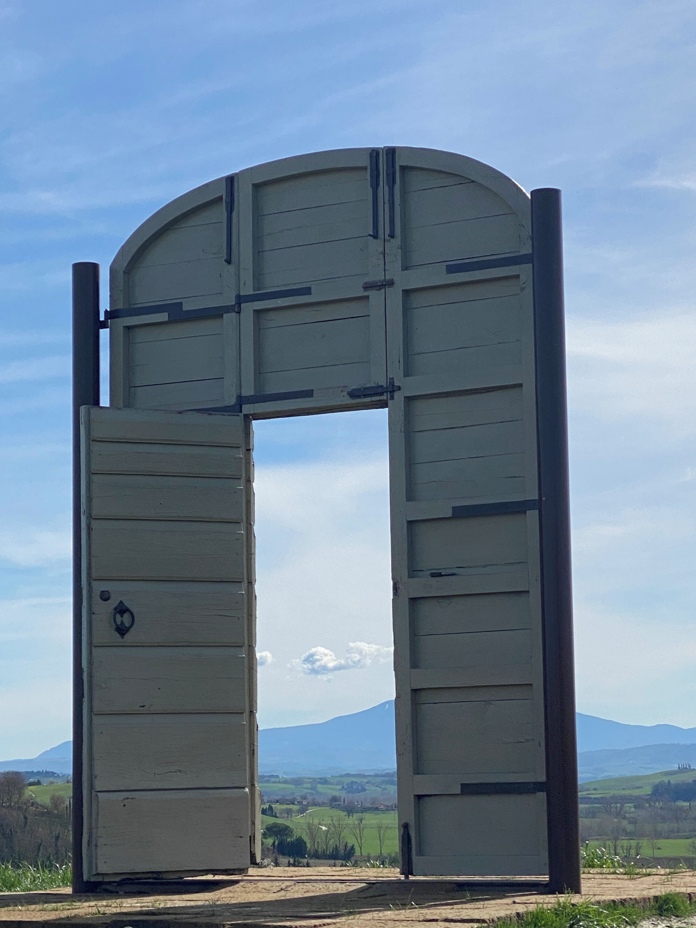 A large wooden gate with a metal frame, set against a backdrop of a clear sky and distant mountains.