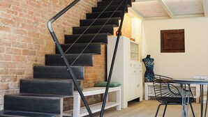Eine Treppe mit schwarzen Stufen und einem Metallgeländer führt zu einer Erkerzone mit weißer Decke und freiliegenden Balken.