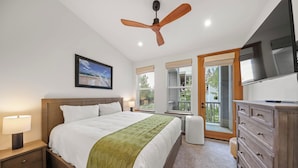 Ein Schlafzimmer mit Bett, Deckenventilator, Fernseher, Kommode und einem Fenster mit Blick ins Freie.