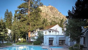 Ein Schwimmbad mit Bergblick, umgeben von Bäumen und einem Gebäude mit weißer Fassade.