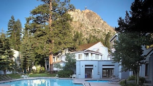 Ein Schwimmbad mit Bergblick, umgeben von Bäumen und einem Gebäude mit weißer Fassade.