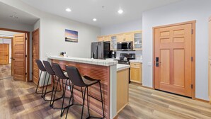 A modern kitchen with a central island, bar stools, stainless steel appliances, and wooden cabinetry. - 705 | King-Sized Comfort - 2BD, Pool, Kitchen W/D (Olympic Valley)