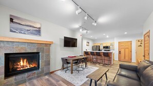 A modern living room with a fireplace, a dining area, a kitchen, and a seating area. - 705 | King-Sized Comfort - 2BD, Pool, Kitchen W/D (Olympic Valley)
