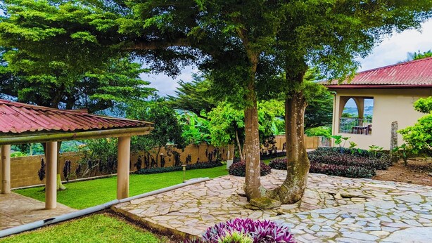 A courtyard with a stone pathway, a pergola, and a building with a red roof. - Charming 3-bedroom house in enchanting Aburi with WiFi, AC (Aburi)