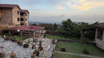 A courtyard with stone flooring, potted plants, and a view of distant buildings under a cloudy sky.