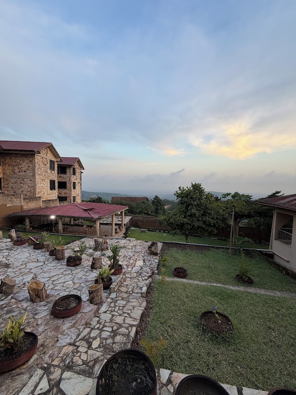 A courtyard with stone flooring, potted plants, and a view of distant buildings under a cloudy sky.
