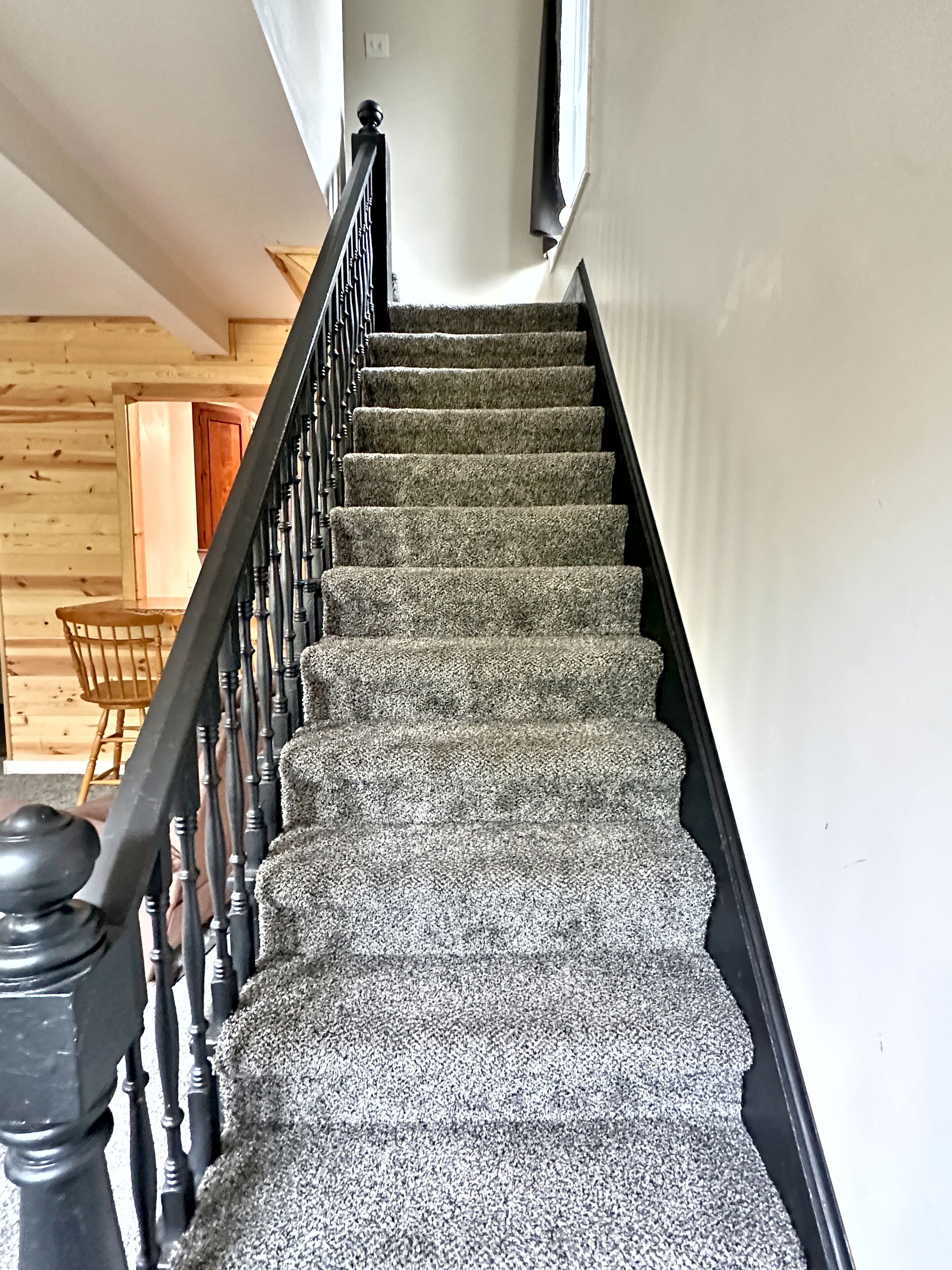 Una escalera con barandilla negra y peldaños alfombrados que conduce a una habitación con paredes de madera y un sillón.