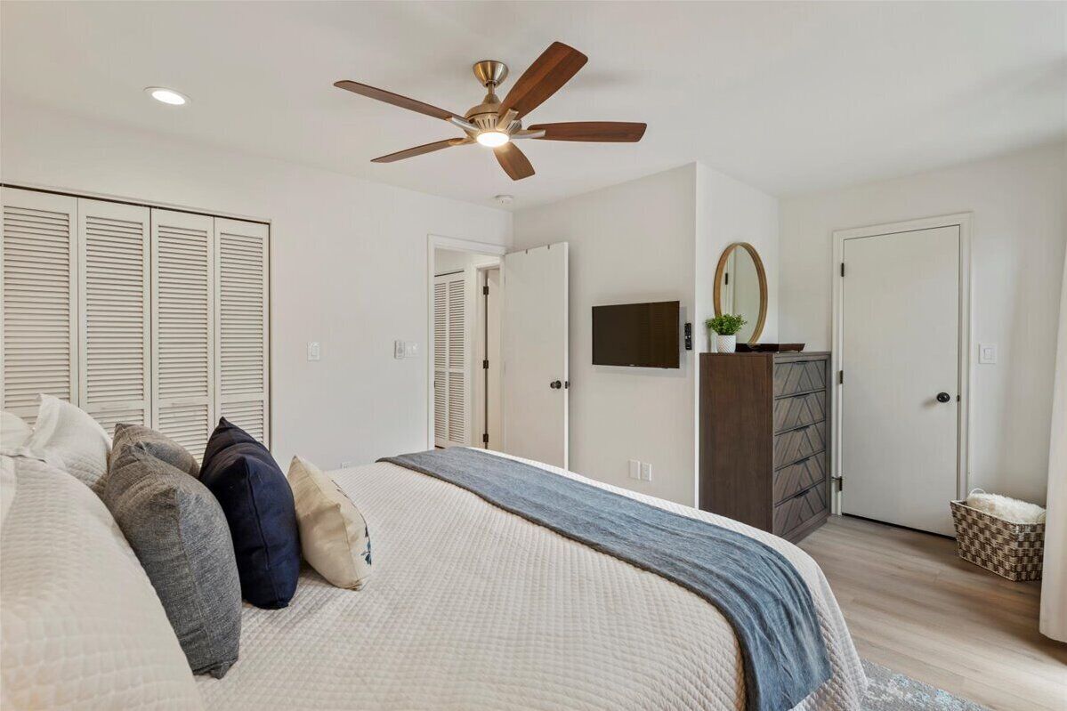 A bedroom with a bed, a ceiling fan, a dresser, and a TV.