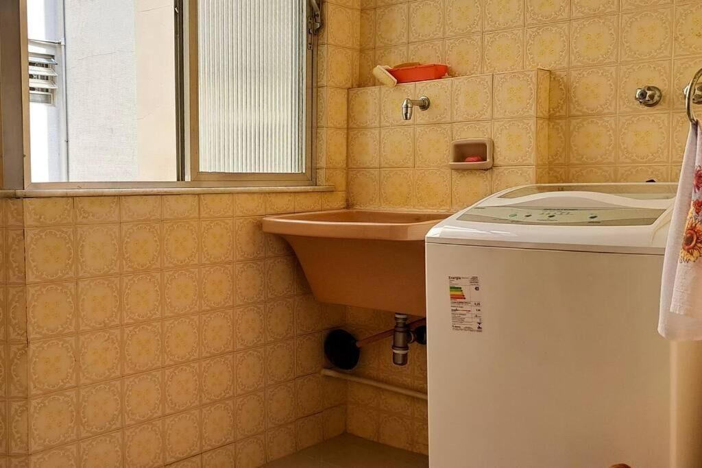 A compact bathroom with a sink, a washing machine, and a window with blinds.