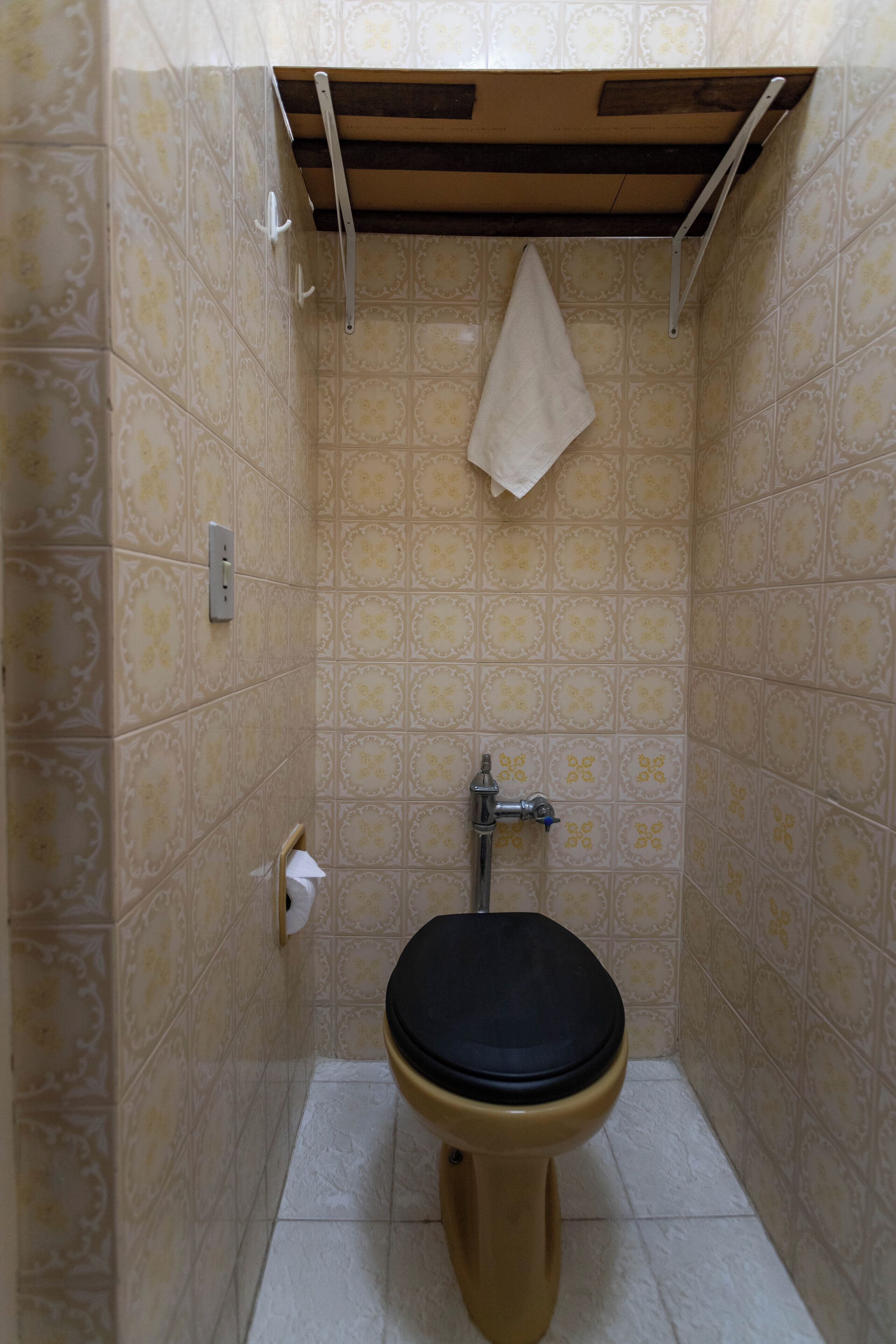A small, tiled bathroom with a toilet, a towel hanging on a rack, and a paper towel dispenser.