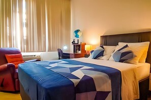 A hotel room with a large bed, a desk, a chair, and a globe on the wall.