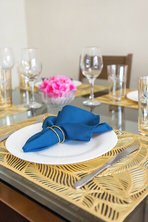 A dining table with a white plate, a blue napkin, and a gold-patterned table runner.