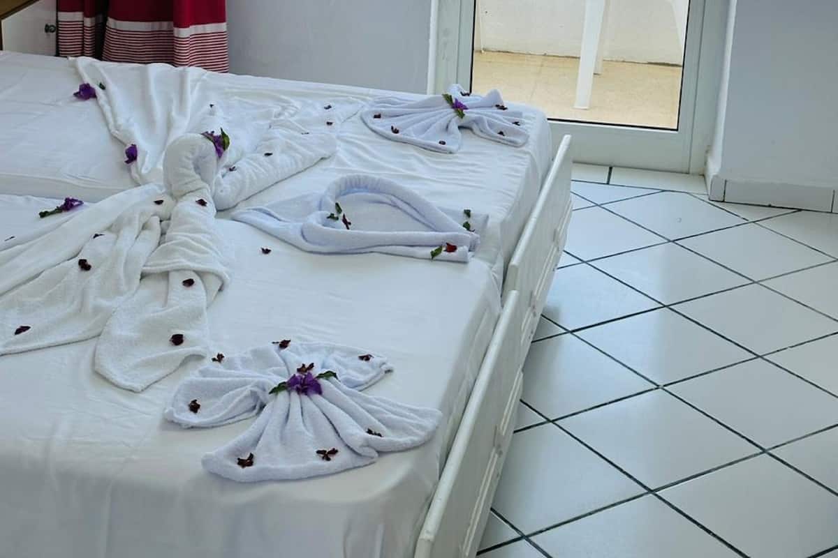 A hotel room with a bed, a view of the beach, and a white chair by the window.