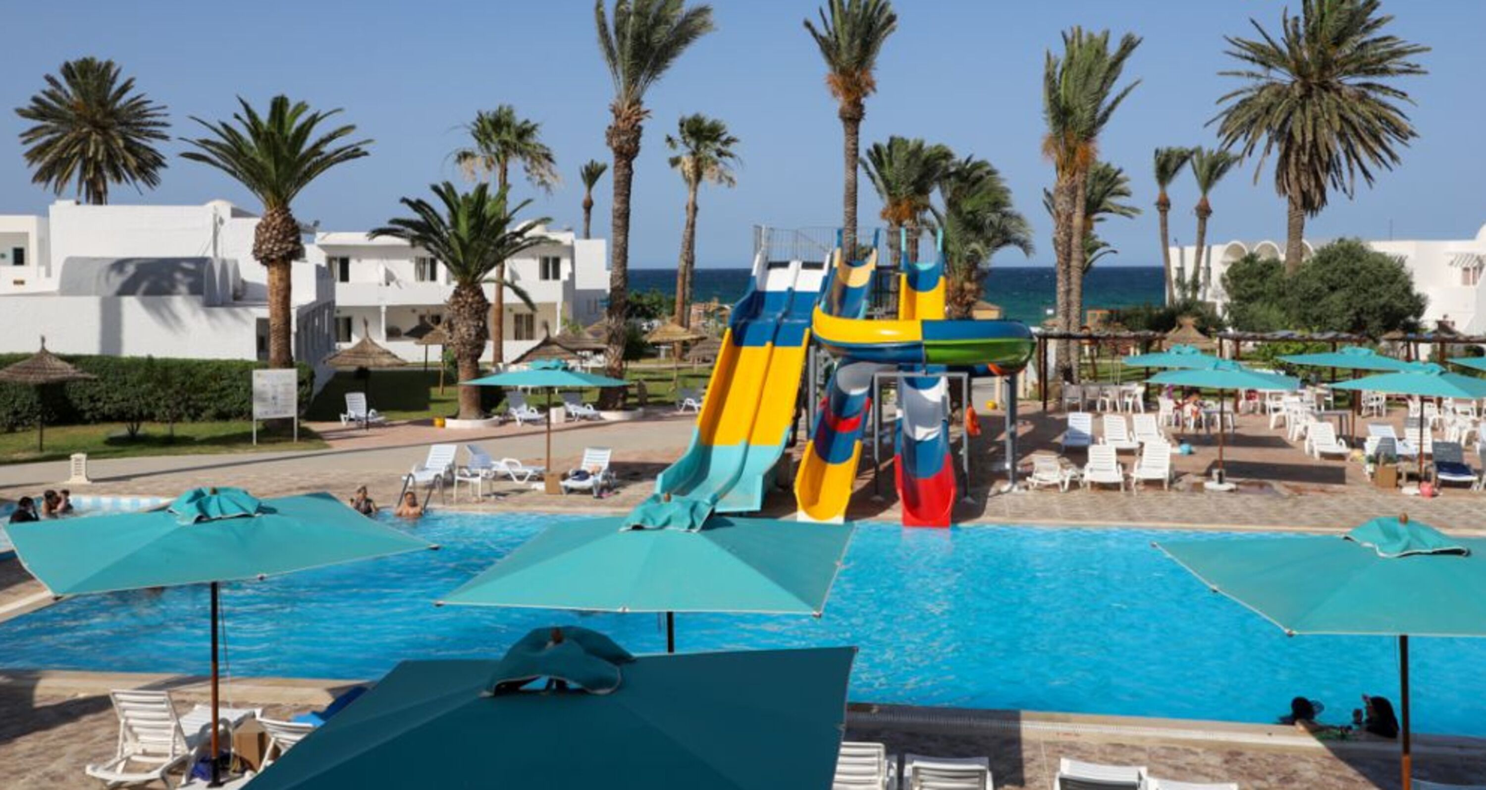 A pool area with multiple slides, lounge chairs, umbrellas, and palm trees.
