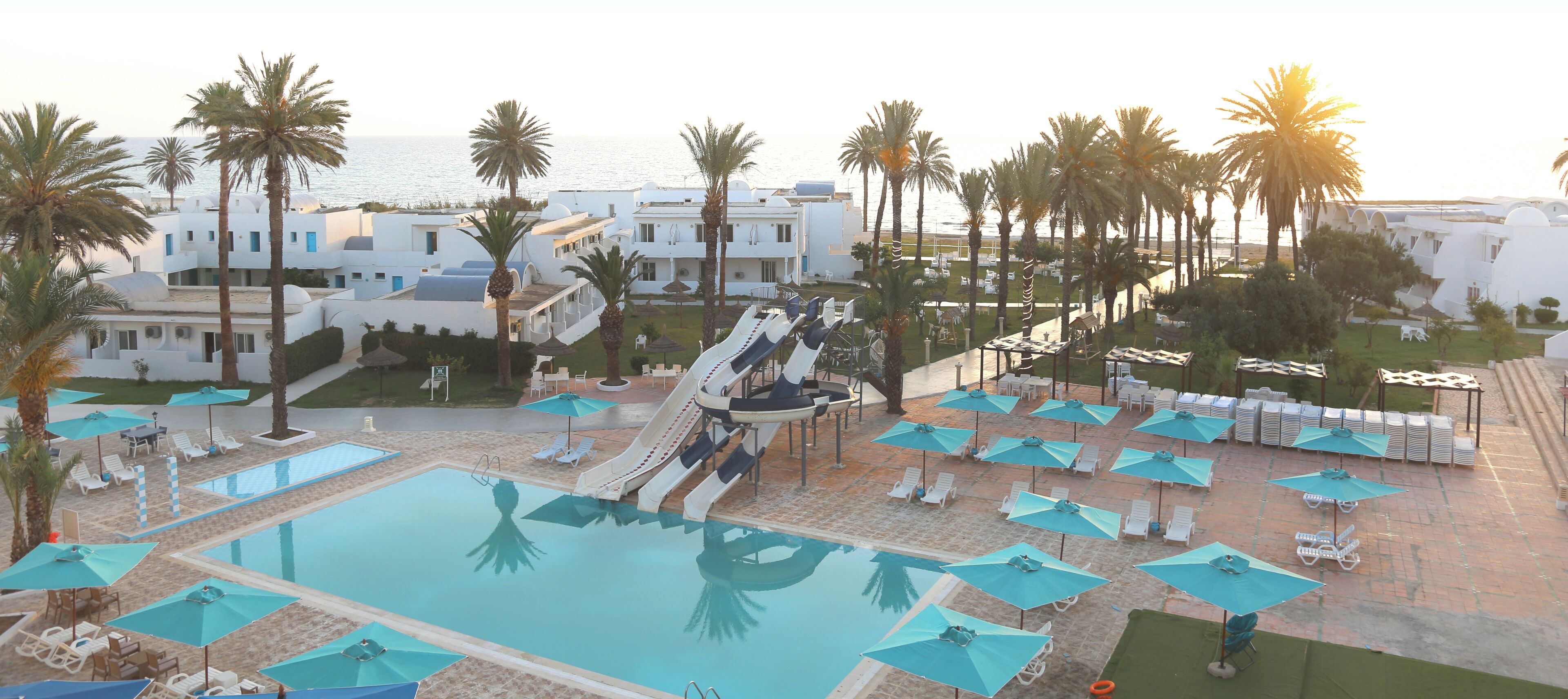Un complexe hôtelier doté d’une piscine, de chaises longues, de palmiers et d’un toboggan.